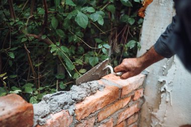 Tuğla ustası tuğlaları havan, macun bıçağı ve malayla yerleştiriyor ve ayarlıyor. Dış duvar inşa eden profesyonel inşaat işçisi