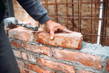 Profesyonel inşaat işçisi endüstriyel inşaat sahasına tuğla döşeyip duvar örüyor. Tuğlayı ayarlamanın ayrıntıları
