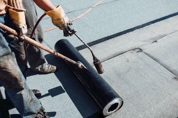 Workers waterproofing flat concrete roof using blowtorch and bituminous membrane rolls