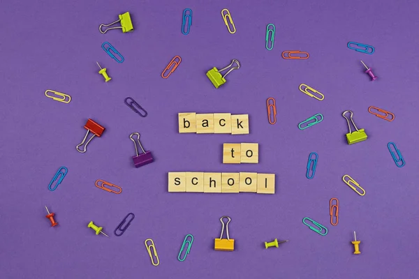 BACK TO SCHOOL text on wooden letters on violet background with colorful stationery items. Concept for beginning of academic year