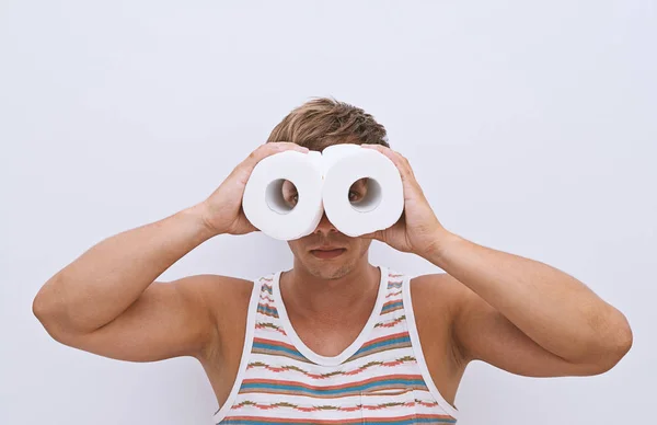 Handsome guy looks through rolls of toilet paper and simulating binoculars. Finding solutions to health problems concept, isolated on white background