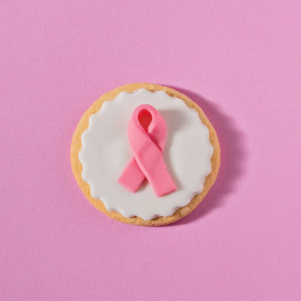 Close up cookies with pink ribbon as sign of the fight against breast cancer on pink background. Concept of International Cancer Day 4 February, flat lay greeting card, square format