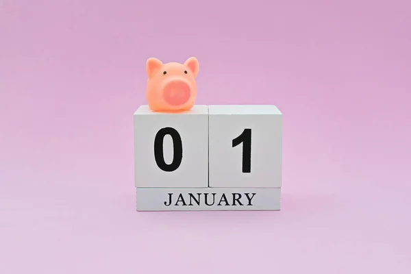1st January is first day of date of financial year start. Cute little piggy on wooden vintage calendar on pink background. New year plans and beginnings concept and tax time, minimal style