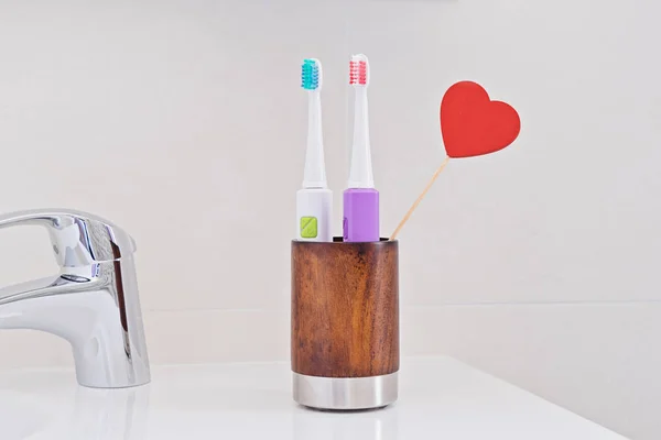 浴室水槽的木玻璃中的两把电动牙刷 心胸红 用于个人医疗保健牙科护理的牙刷 口腔牙科卫生 牙科设备 早晨常规概念 — 图库照片
