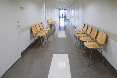 Birçok beyaz kabine kapılar ve hafif ahşap boş sandalyeler Polikliniği koridor görünümü.