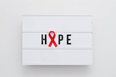 Kırmızı kurdele umudun simgesi ve AIDS ve kanser farkındalığı. Metin umut ile ışık kutusu ve kırmızı kurdele kavramı Uluslararası Kanser günü ve Dünya AIDS Günü olarak