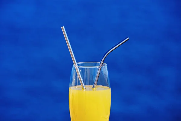 Fechar de beber vidro com suco de laranja e palhas metálicas contra azul — Fotografia de Stock