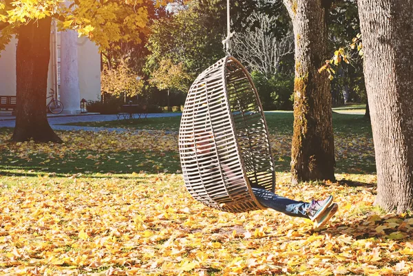 Girl in autumn park swinging on hanging rattan chair