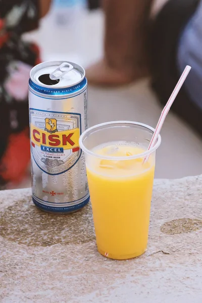 Lata de cerveja maltês local Cisk lager e suco de laranja em copo de plástico — Fotografia de Stock