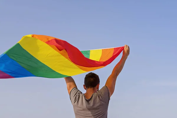 Homem segurando as mãos levantadas acenando bandeira do arco-íris LGBT — Fotografia de Stock