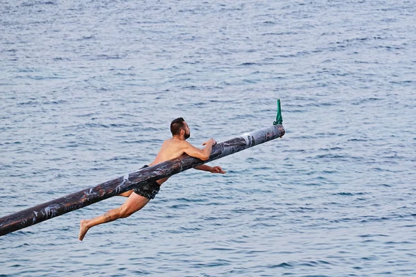 Competitor tries to grab flag on Gostra on wooden pole covered in grease and fat — Stock Photo, Image