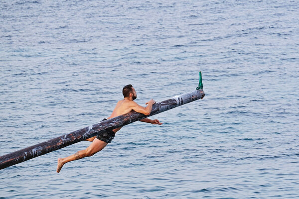 Competitor tries to grab flag on Gostra on wooden pole covered in grease and fat