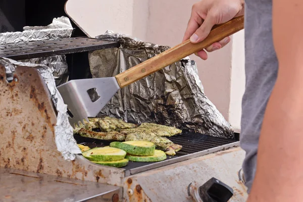 Man cooking steaks and zucchini medallions are cooked on gas-grill grate