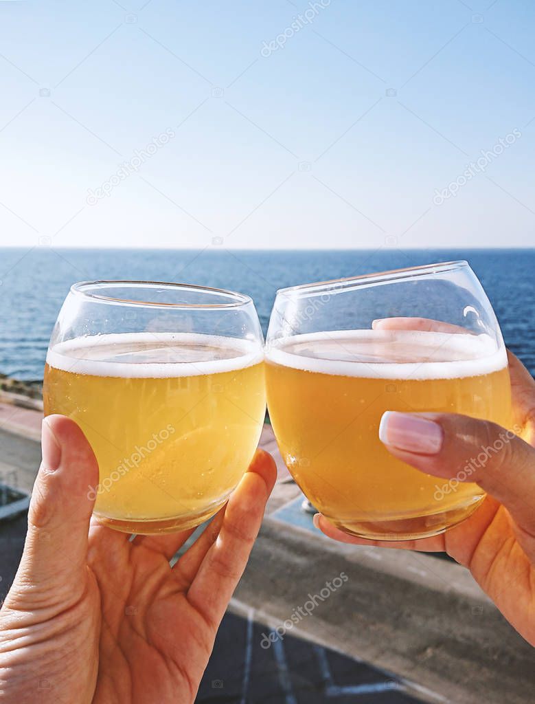 Hands holding glasses with cold beer against blue sky, closeup view