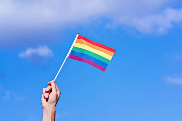 Raised hand with waving LGBTQ rainbow flag against blue sky. Annual LGBT Pride Celebration