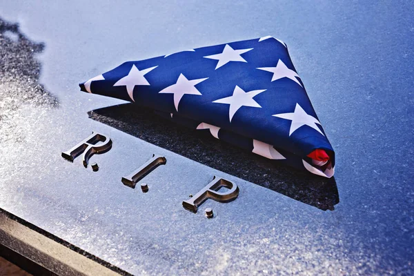 Folded into triangle American flag on memorial marble tomb with R.I.P. text. Flag folding ceremony is way to honor flag on special days, like Memorial Day or Veteran\'s Day