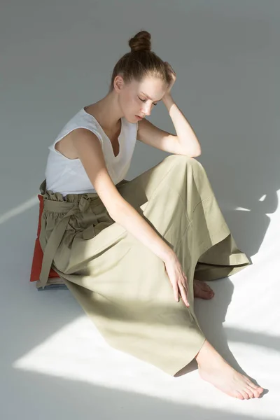 スタジオの床に若い女性が座っている 彼女は長い緑のスカートと白い夏のタンクの上を着ています 目が閉じている 天然化粧 — ストック写真