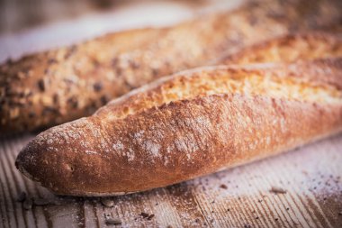 Yakından bakınca ayçiçeği tohumlu taze baget ekmeği ve kırsal ahşap masadaki diğer tohumlar ve un istirahatı görülüyor.