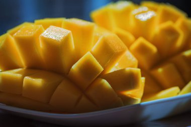 Doğal Taze Olgun Mango küpleri, Dilimler yakın çekim, Makro çekim. Koyu mavi ya da siyah arka planda. Kırsal ahşap tahtada ve bambu peçetede