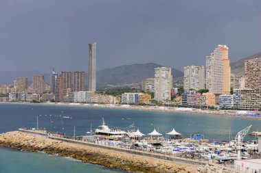Benidorm Poniente sahilinin Benidorm, Alicante, İspanya 'daki liman, gökdelenler, botlar ve dağların manzarası.