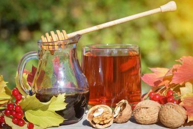 Bardakta sıcak bitki çayı, karabuğday balı, cevizli taze elma ve kırsal güvertede viburnum üzümü. Sonbahar sakin bir hayat.