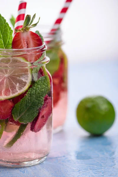 Limonlu ve çilekli detoks içeceklerin mavi arka plandaki cam mason kavanozlarıyla yakın plan görüntüsü. Sağlıklı yaz limonatası..