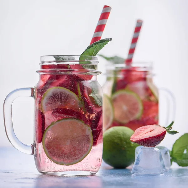 Limonlu ve çilekli detoks içeceklerin mavi arka plandaki cam mason kavanozlarıyla yakın plan görüntüsü. Sağlıklı yaz limonatası..