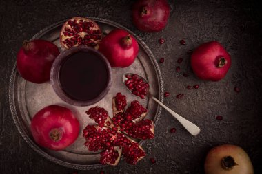 Gümüş tepside bir bardakta nar suyu ve etrafa saçılmış tohumlar serpiştirilmiş taze nar. 3