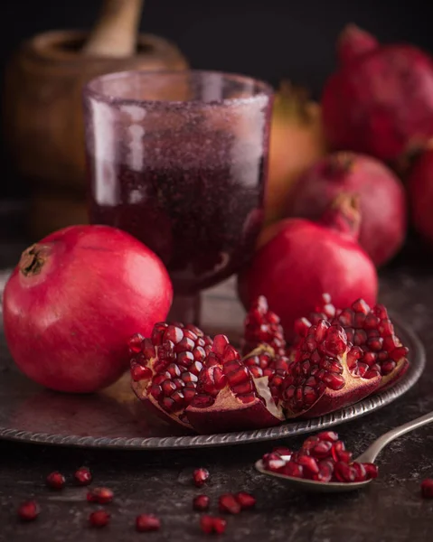 Pomegranate juice in a glass on the silver tray with fresh pomegranates around with scattered seeds low key. 5