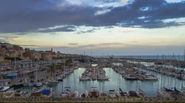Gün batımında Montgat yat limanındaki demirli yelkenlilerin hava panoramik manzarası dramatik bulutlu gökyüzü ve hala durgun su. Barselona, İspanya.