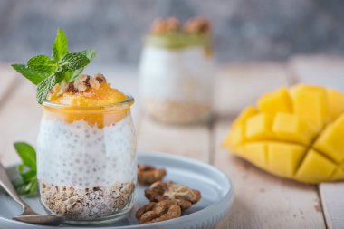 Ev yapımı Chia tohumu ve badem sütü mısır gevreği, mango püresi ve cevizli kivi ve cam kavanozlarda naneli. Vejetaryen sağlıklı sabah kahvaltısı veya kırsal ahşap masada süper yiyecek tatlısı..