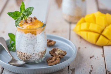Ev yapımı Chia tohumu ve badem sütü mısır gevreği, mango püresi ve cevizli kivi ve cam kavanozlarda naneli. Vejetaryen sağlıklı sabah kahvaltısı veya kırsal ahşap masada süper yiyecek tatlısı..