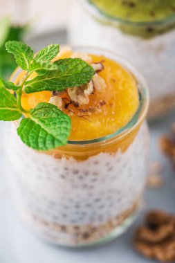 Ev yapımı Chia tohumu pudingi ve badem sütü mısır gevreği, mango püresi ve cevizli kivi ve cam kavanozlarda naneli. Vejetaryen sağlıklı sabah kahvaltısı ya da beyaz tabakta süper yemek tatlısı.