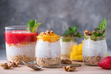 Ev yapımı Chia tohumu ve badem sütü ile mısır gevreği, kivi püresi, çilek ve ceviz ve nane şekerli cam kavanozlar. Vejetaryen sağlıklı sabah kahvaltısı ya da ahşap masada süper yiyecek tatlısı..