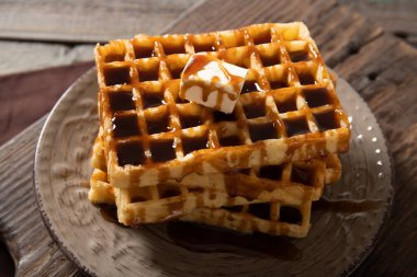 Lezzetli waffle ve karamel sosu ile bir dilim tereyağı. Ahşap bir arka planda