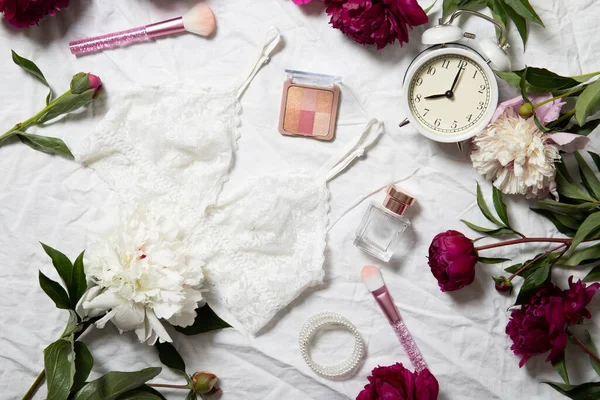 Beautiful peonies, alarm clock and cosmetics on a white background. View from above