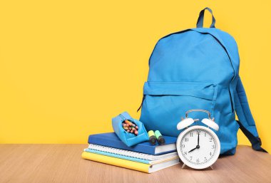 Sarı arka planda mavi sırt çantası ve kırtasiye malzemesi, mesaj için yer. Öğrenme kavramı