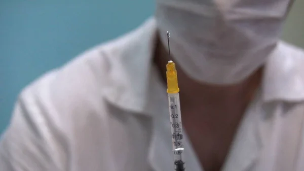 Elinde şırıngayla maskeli doktor iğneye hazırlanıyor.