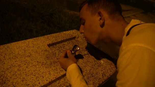 a young guy drinks water from a fountain in the evening