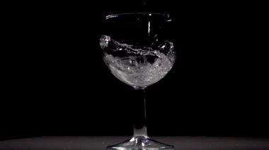 Yavaş çekim siyah arka plan üzerinde şarap cam içine su dökme