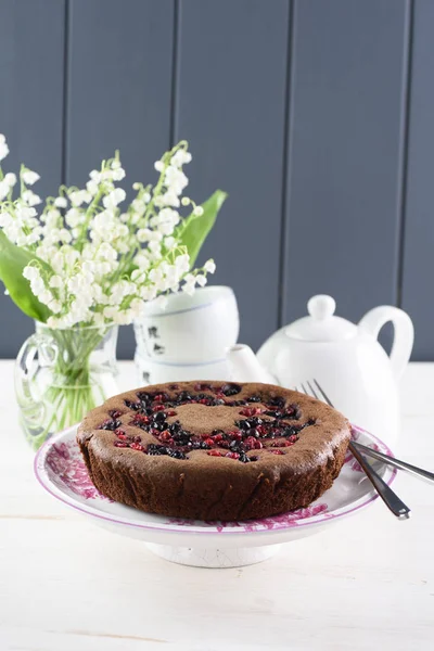 Homemade chocolate berry cake with bird cherry flour. Tasty bird cherry cake served with white teaware and lily of the valley flowers and copyspace