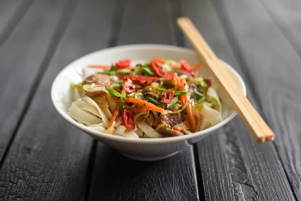 Traditional Asian noodles minimalist style. Stir fry udon noodles with meat, vegetables, chili and spring onion on burnt black background  with perspective