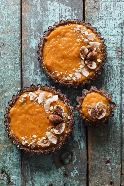 Raw vegan dessert for family. Pumpkin tarts with nut and oatmeal crust on old blue table above view