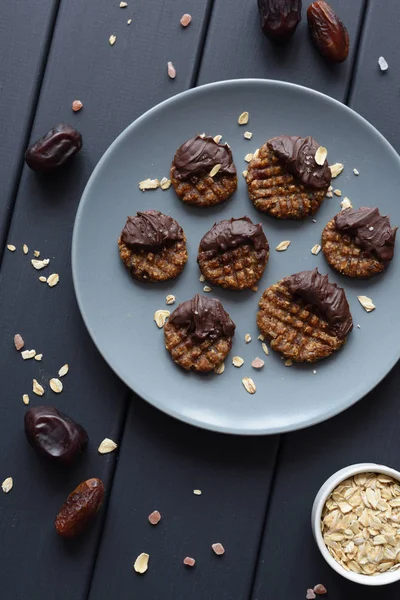 Raw vegan gluten free cookies with chocolate glaze served with ingredients: oats, dates and himalayan salt on grey plate top view