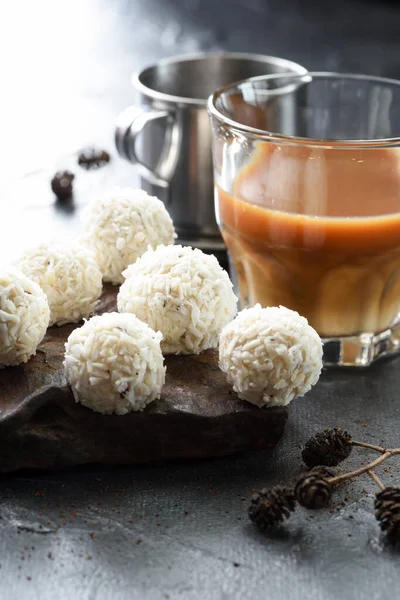 Sweet energy balls with coconut flakes in pile on dark stone with milk phin coffee on black plaster background