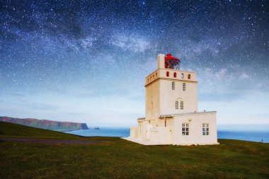 Fantastik yıldızlı gökyüzü ve Samanyolu. Dramatik ve güzel sahne. Güzel beyaz deniz feneri Cape Dyrholaey, South Iceland.