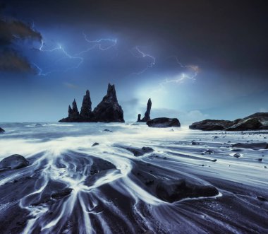 Bulutlu karanlık Gökte şimşek. Yıllık fantastik gece sahne. Rock Troll ayak parmakları. Reynisdranhar taş. Siyah kum plaj. İzlanda.