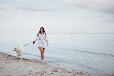 Yürüyen bir köpek ile sahilde güzel esmer kadın.
