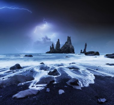 Bulutlu karanlık Gökte şimşek. Yıllık fantastik gece sahne. Rock Troll ayak parmakları. Reynisdranhar taş. Siyah kum plaj. İzlanda.