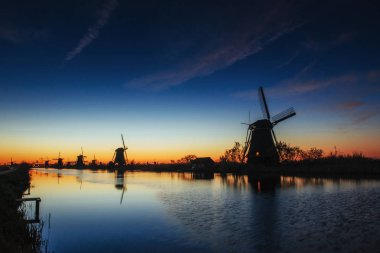 Renkli bahar günbatımı geleneksel Hollanda Rotterdam kanalda yel değirmenleri. Ahşap iskele göl kıyıya yakın. Holland. Hollanda.
